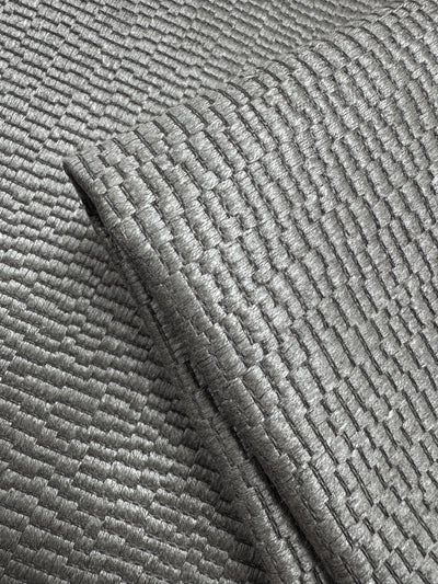 Close-up of Super Cheap Fabrics' Upholstery Jacquard - Oscar Putty (148cm): a shiny, silver-gray heavyweight fabric with a geometric basket-weave pattern that reflects light, showcasing its intricate weave and metallic look.