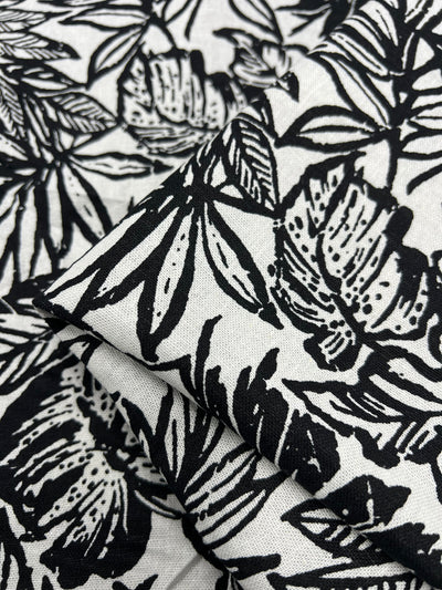 Natural fiber linen fabric featuring an elegant assortment of leafy patterns, artfully printed in black ink against a crisp white backdrop. Ideal for sophisticated home decor and fashion projects.