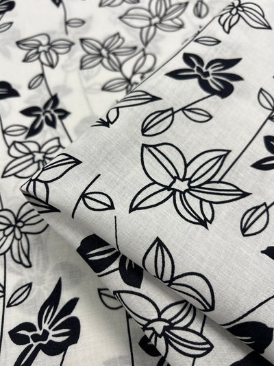 Lightweight linen fabric featuring an elegant black and white stencil print of lotus flowers, perfect for creating stylish and breathable garments. Ideal for fashion-forward individuals looking to make a statement.
