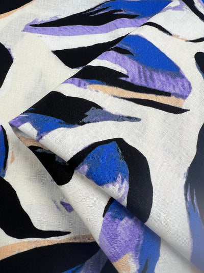 Soft, natural fiber linen fabric featuring an elegant blue-purple and black petal-like print on a white background. Ideal for creating luxurious clothing and home decor items that stand out. Perfect for those looking to add a touch of sophistication and natural beauty to their products.