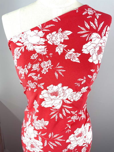 A mannequin displays Super Cheap Fabrics' Printed Lycra - Cherry Flora (150cm), a red polyester spandex with white floral print, styled one-shoulder on a light gray background.