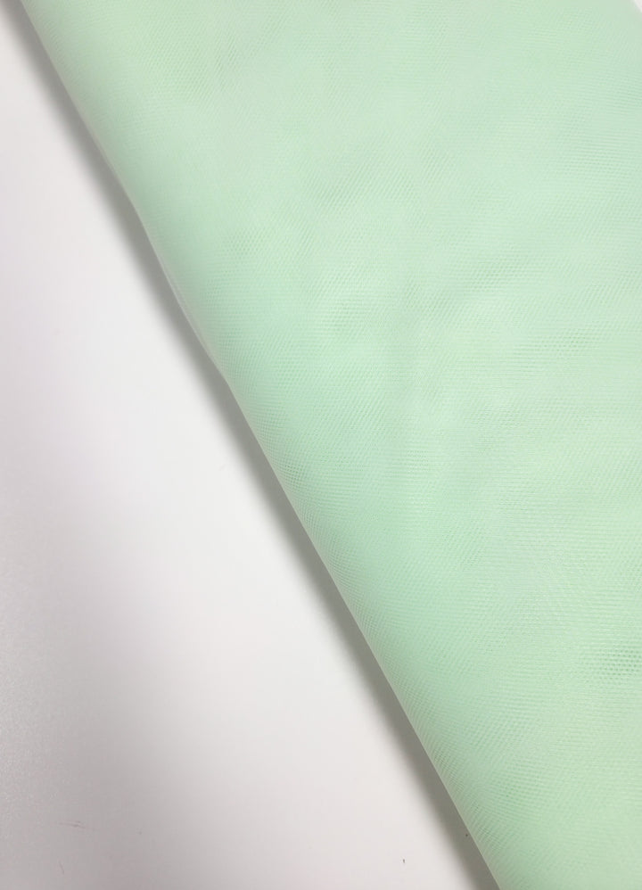 Super Cheap Fabrics’ Soft Tulle - Patina Green - 150cm is a soft, subtly textured and slightly translucent fabric, ideal for bridal veils or costumes. Shown here partially unrolled on a white surface.