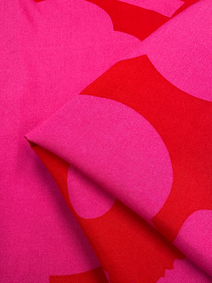 Close-up of Designer Rayon - Jam Poppy (145cm) by Super Cheap Fabrics, featuring bold abstract pink and red patterns with large circles and geometric shapes on smooth, lightweight rayon—ideal for vibrant prints.