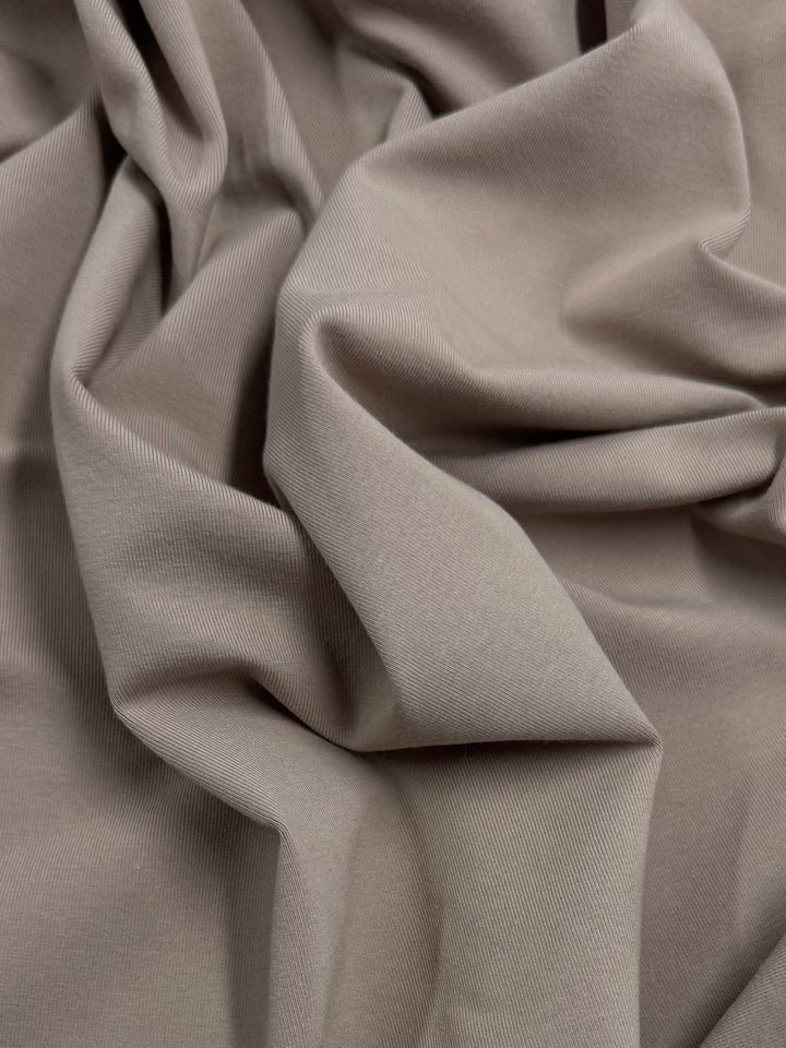 A close-up of Super Cheap Fabrics' Cotton Lycra - Mocha Meringue - 170cm reveals gentle folds, smooth texture, slight sheen, and stretch in its soft beige fabric.