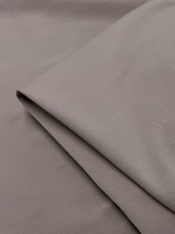 A close-up of Super Cheap Fabrics' Cotton Lycra - Mocha Meringue (170cm) shows its smooth, medium-weight, light brown material with a folded section over a flat piece.