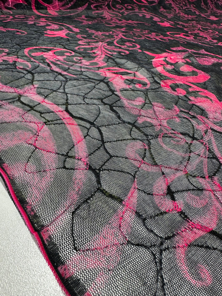 The Designer Mesh - Delicate - 150cm by Super Cheap Fabrics features lightweight polyester with intricate pink floral and swirl patterns on black netted mesh, offering sheer, decorative textures that create a striking contrast.