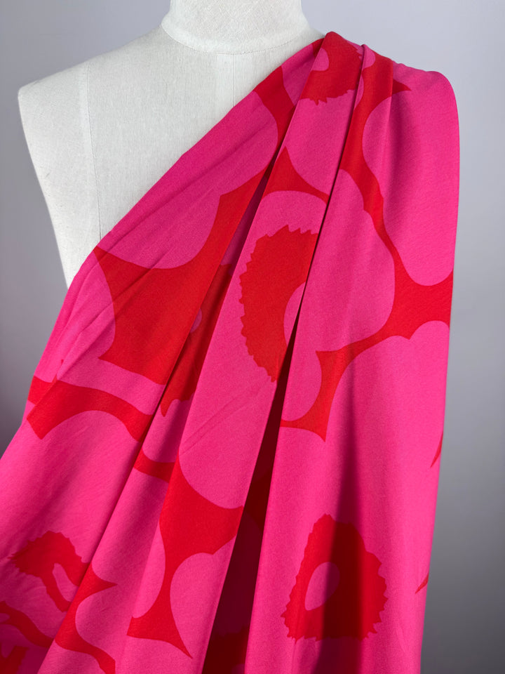 A mannequin displays Super Cheap Fabrics’ Designer Rayon - Jam Poppy (145cm), a bright pink fabric with bold abstract red floral prints flowing diagonally across the chest—perfect for versatile, creative styling.