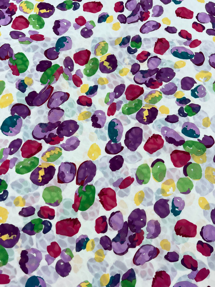 The Salt Shrunk Print - Pebbly from Super Cheap Fabrics features vibrant clusters of abstract shapes in purple, green, yellow, and pink on a white background, resembling scattered paint splotches.