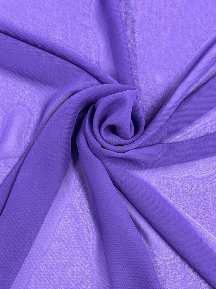 A close-up of the Hi-Multi Chiffon - Pansy by Super Cheap Fabrics, artistically arranged in swirling folds to form a spiral. This sheer, lightweight fabric is 150cm wide and displays a smooth texture with a slight sheen.