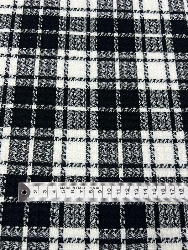 A close-up image of black and white plaid fabric, identified as "Designer Tweed - Chanel - 145cm" from Super Cheap Fabrics, with a small ruler laying on top. The ruler shows measurements in centimeters, ranging from 0 to 15. The fabric's intricate checkered pattern is prominently displayed.