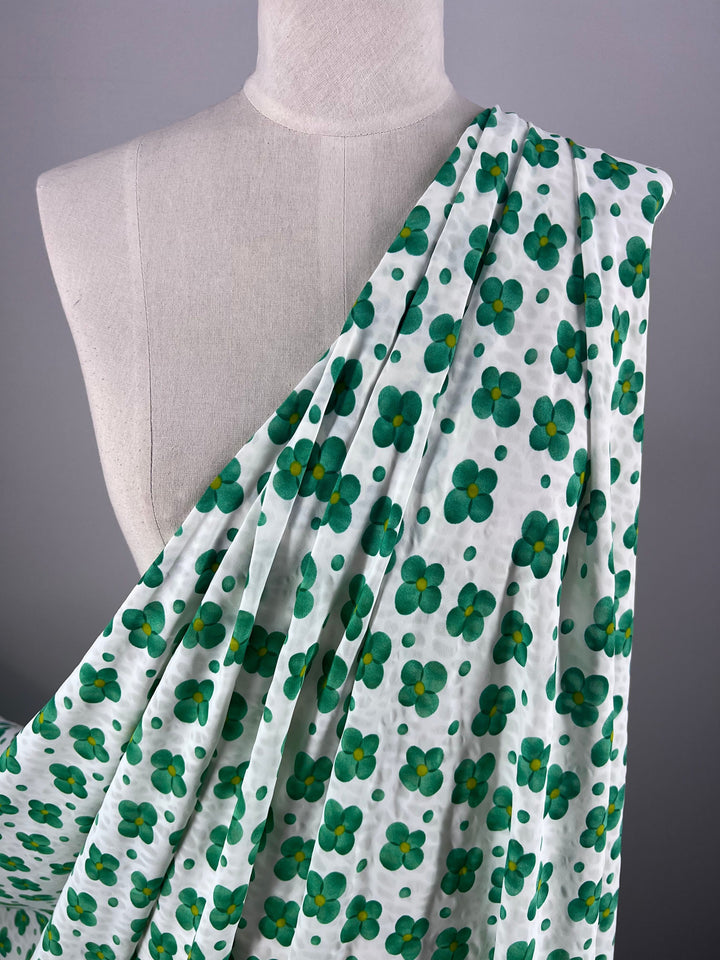 A dressmaker's mannequin draped with Super Cheap Fabrics' Salt Shrunk Print - Clover (155cm), showcasing vibrant green and teal flowers, asymmetrically arranged over one shoulder against a plain gray background.