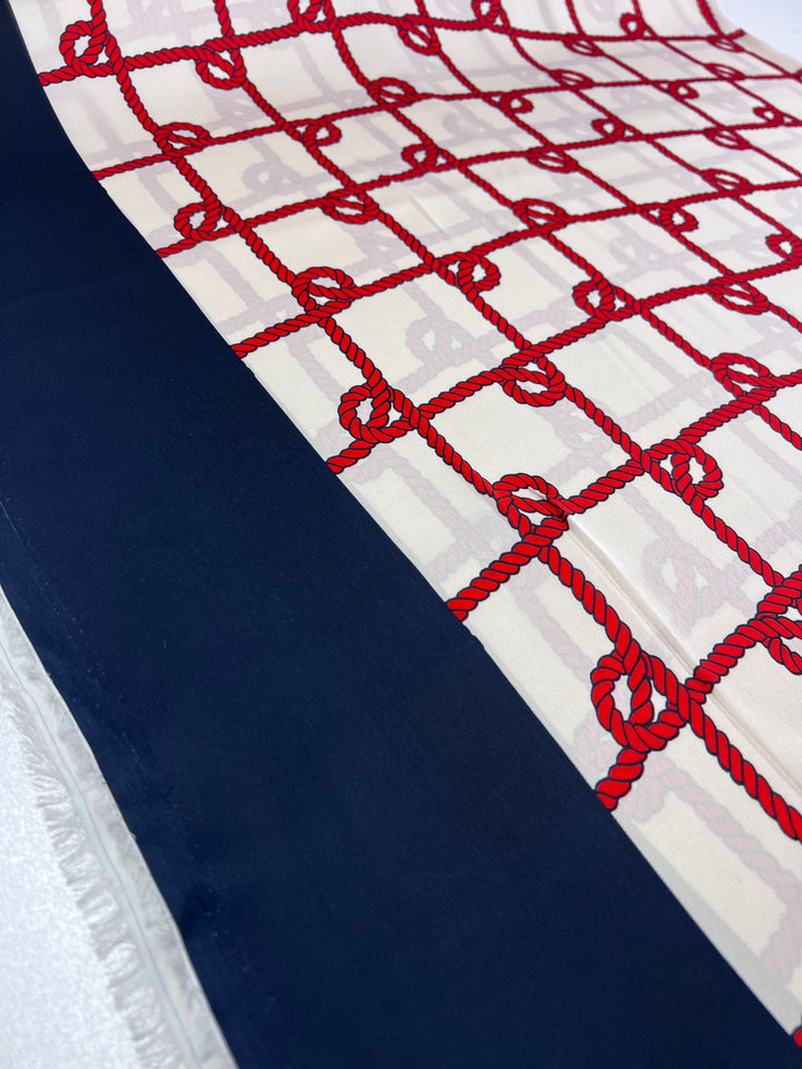 A close-up of Super Cheap Fabrics' Printed Satin - Cruise shows an elegant nautical design with red ropes in a grid on white and a striking dark blue border, 150cm wide.