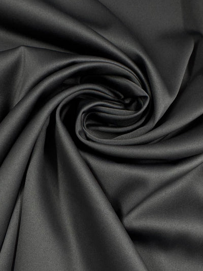 A close-up of Super Cheap Fabrics' Satin Deluxe in Charcoal (150cm) reveals its smooth, lightweight polyester satin twisted into a spiral, showcasing its soft, silky texture with subtle highlights and shadows.