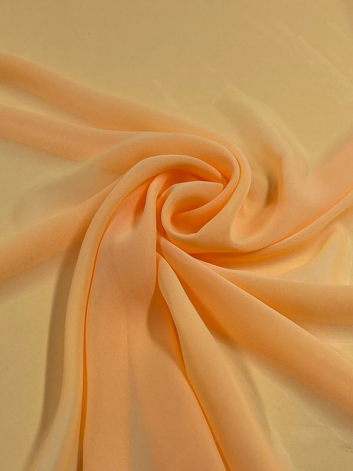 A photo shows Super Cheap Fabrics' Hi-Multi Chiffon in Marigold, 150cm wide, arranged in a swirl. The sheer, marigold hue fabric creates a delicate and airy look with its transparency and soft flow.