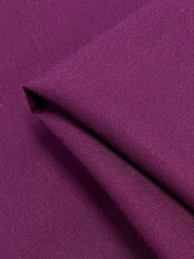 Super Cheap Fabrics' Plain Rayon in magenta boasts a double folded, smooth-textured surface. This 100% Rayon fabric is lightweight with a medium thickness and closely woven construction, presenting a solid, even matte finish. The vibrant purple hue adds a rich touch to its appearance and measures 140cm in width.