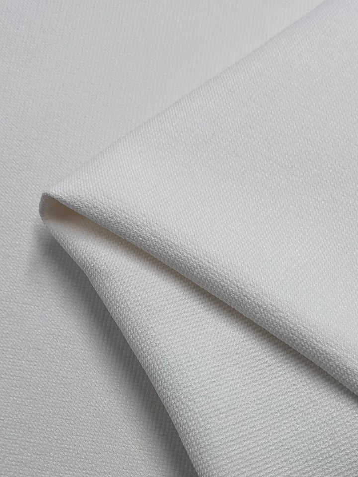 A close-up of the Hopsack Suiting - Ivory by Super Cheap Fabrics shows folded fabric with a textured surface, highlighting its smooth finish, softness, light color, and versatility.