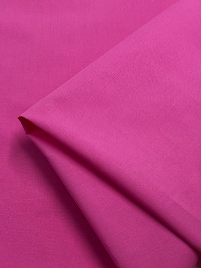 A beautifully folded piece of Plain Cotton - Pink Power - 156cm from Super Cheap Fabrics sits against a matching pink background. This lightweight fabric showcases its smooth texture and vibrant, uniform pink color.