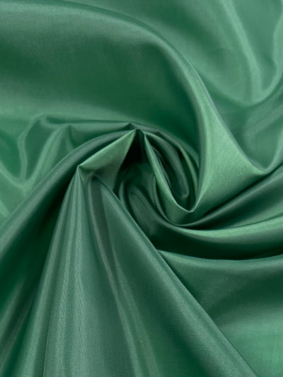 Close-up of smooth, green fabric with soft folds and gentle ripples, creating a flowing, luxurious texture. The lightweight fabric has a slight sheen, emphasizing the richness and quality of the material — ideal as a garment accent or Super Cheap Fabrics' Lining - Formal Garden - 150cm polyester lining.