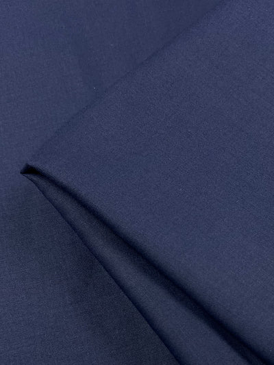 A close-up of folded **Superfine Suiting - Navy - 150cm** by **Super Cheap Fabrics** in a wool polyester blend. The texture appears smooth and tightly woven, with the light creating subtle variations in the shade of blue. The fabric is neatly arranged, showcasing its clean lines and deep color.