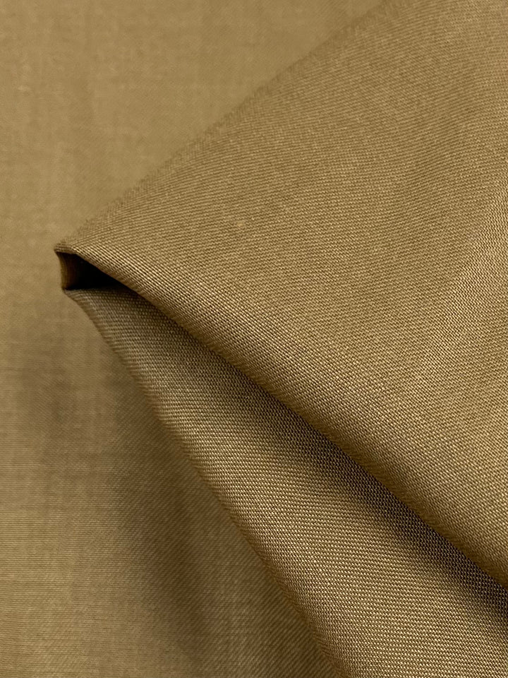 A close-up view of a folded piece of Superfine Suiting - Bronze Brown - 150cm by Super Cheap Fabrics. The texture appears smooth, and the fabric is neatly creased, suggesting it is possibly made of cotton or a similar material. The lighting highlights the fabric's delicate weave pattern.