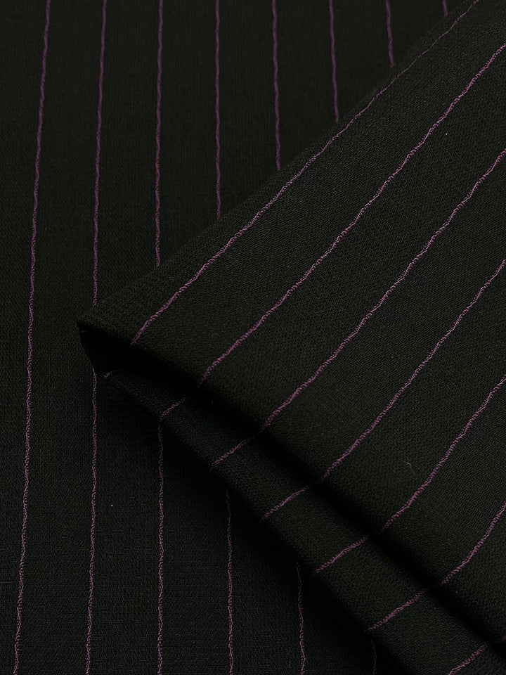 Close-up image of Microfibre Suiting - Black/Pink Stripe fabric, made from medium weight polyester by Super Cheap Fabrics. The fabric appears to be folded, clearly displaying its classic and elegant design with evenly spaced pink pinstripes against a black background. Fabric width is 150cm.