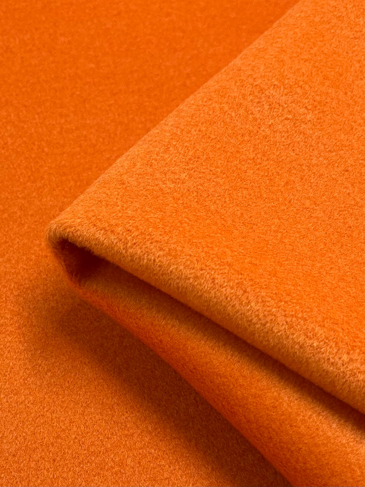 Close-up of an orange fabric folded neatly. The texture appears plush and soft, suitable for clothing or upholstery. This high-quality Wool Cashmere - Carrot from Super Cheap Fabrics emphasizes the warm, vibrant color and the premium quality of the material. Measuring 150cm wide, this fabric is ideal for a variety of elegant projects.