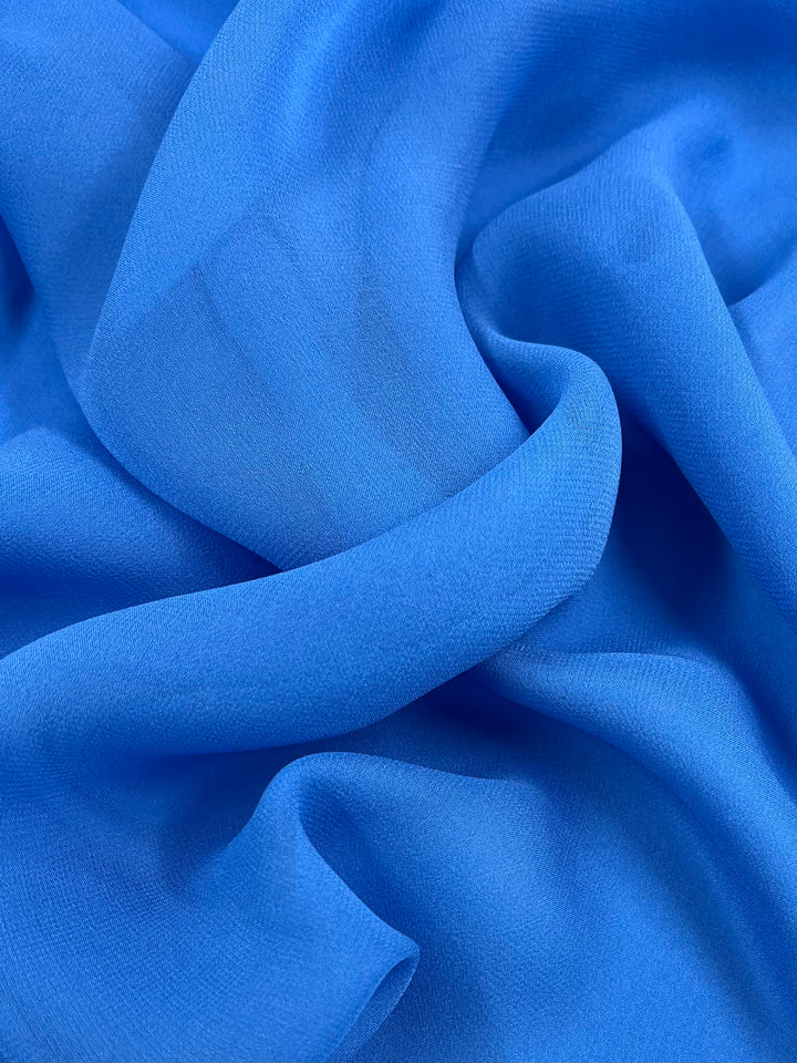 Close-up of Super Cheap Fabrics' Pure Silk Georgette in Denim, 135cm wide, displaying its smooth texture and gentle folds. This lightweight material is soft with subtle shading variations that add depth and movement, ideal for elegant spring-summer outfits.