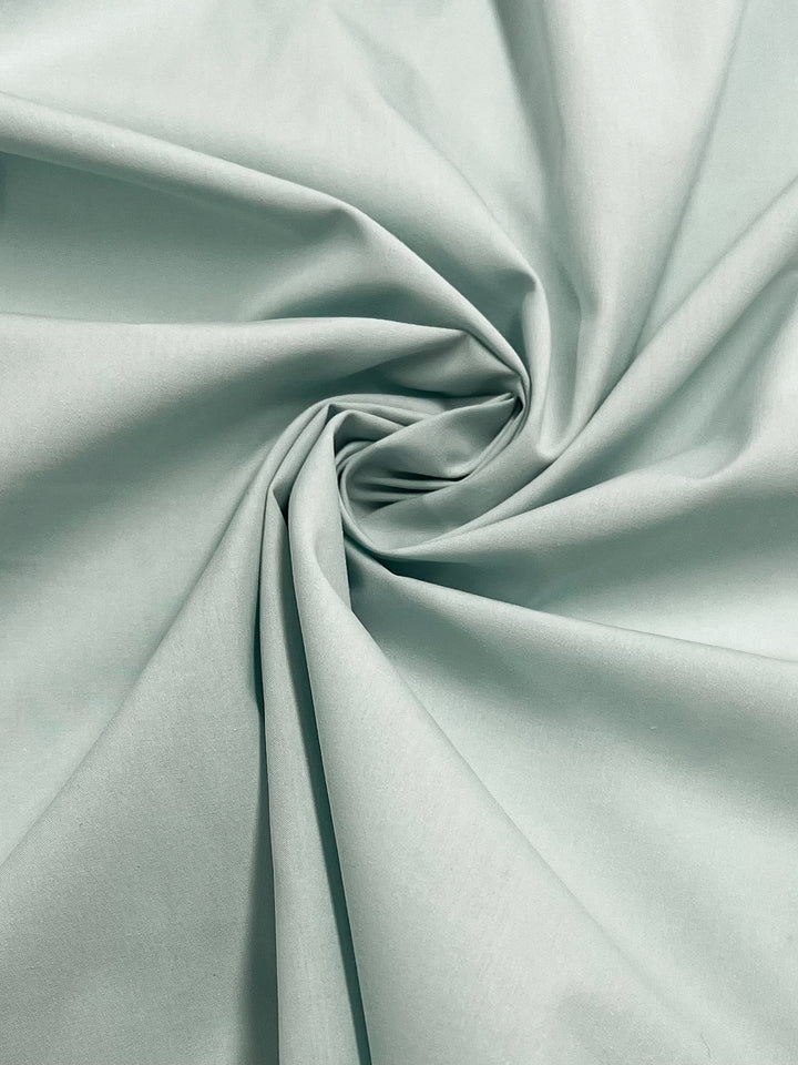 A close-up of Super Cheap Fabrics’ Plain Cotton - Cooling Oasis - 156cm shows light blue or mint green fabric, gathered and twisted into a spiral with soft folds—evoking a refreshing oasis with its cool, lightweight texture.