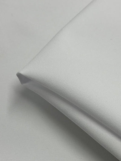 Close-up of a neatly folded piece of medium-weight white fabric on a plain background. The Panama Suiting - White - 150cm by Super Cheap Fabrics has a smooth texture and clean lines, suggesting it could be used for various applications such as clothing or linens.