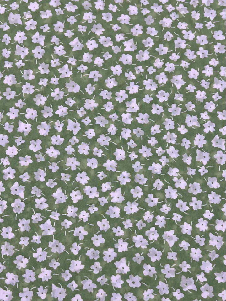 Discover our "Salt Shrunk Print - Jassy - 155cm" from Super Cheap Fabrics, showcasing a vibrant green backdrop adorned with a delicate pattern of small white flowers.