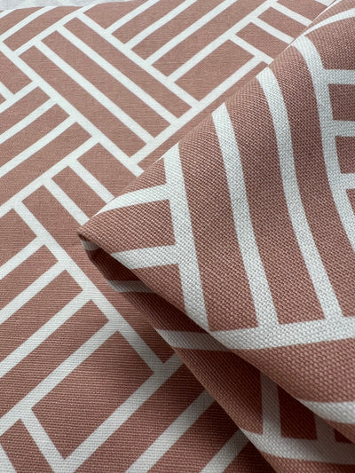 A close-up photo of a cotton fabric with a geometric pattern. The light brown fabric with white lines forms a modern, interlocking rectangular design. Part of the fabric is slightly folded, showcasing the texture and weave in detail—perfect for arts & crafts or home décor projects. This is Printed Canvas - Chopped - 145cm by Super Cheap Fabrics.