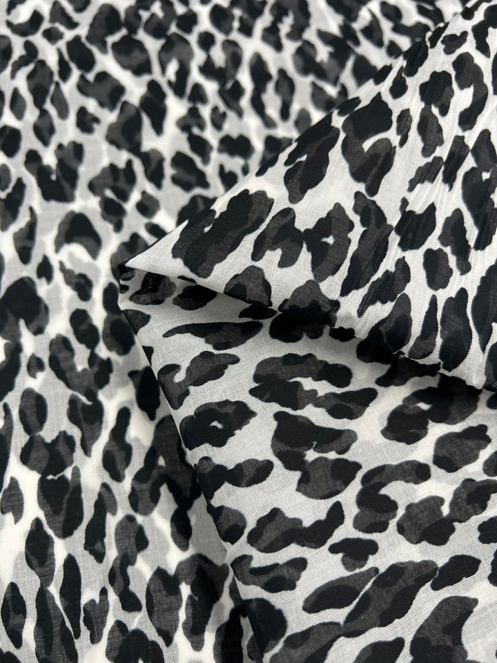 A close-up of the Pure Printed Silk Voile - Snow Leopard - 145cm by Super Cheap Fabrics, displaying a black and white leopard print pattern. The image showcases the texture and design of this extra lightweight silk cotton fabric, ideal for dresses, with one corner slightly folded over.