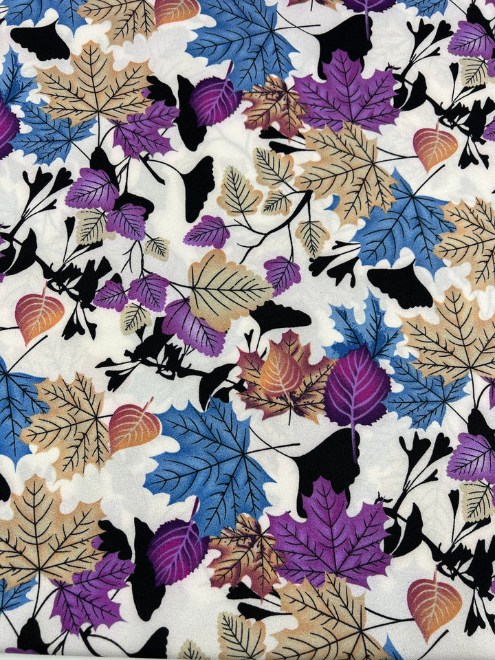 A vibrant polyester fabric pattern featuring an array of leaves in shades of purple, blue, gold, black, and brown scattered across a white background. The lightweight fabric showcases varied leaf shapes and sizes, creating a dynamic and visually engaging design perfect for high fashion. This is the Printed Crepe - Colourful Fall - 150cm from Super Cheap Fabrics.