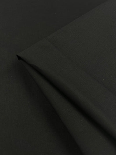 Close-up image of black fabric, showing a folded portion on the right side. The lightweight material appears smooth and slightly matte, with no visible patterns or textures. Cotton Voile - Black - 145cm by Super Cheap Fabrics.