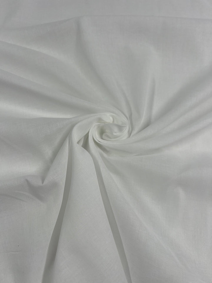 A close-up image of Super Cheap Fabrics' Cotton Voile - White - 145cm, displaying a smooth and slightly shiny surface. The fabric is twisted gently at the center, creating a swirling pattern with soft folds and creases radiating outward—ideal for elegant home decor projects.
