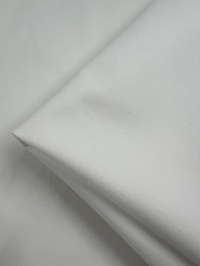 A close-up image of a folded piece of Super Cheap Fabrics Stretch Drill - White - 120cm. The medium weight fabric has a soft appearance with subtle shadows enhancing its texture. The clean, minimalist setup emphasizes the fabric's purity and simplicity.