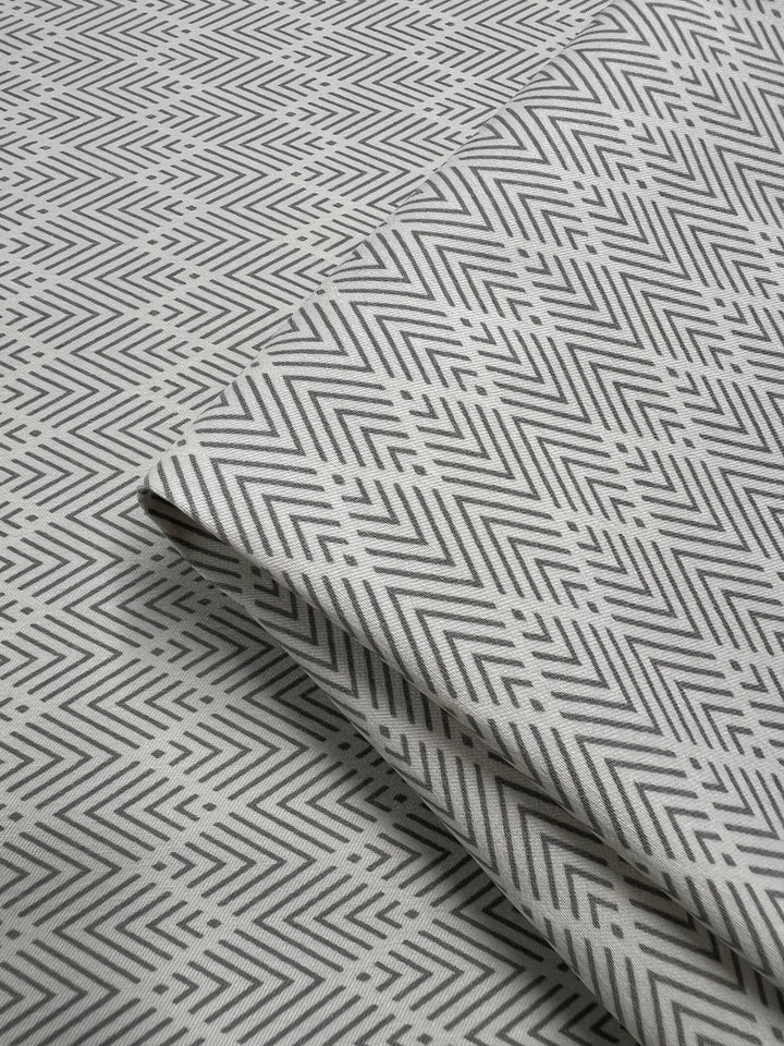 A close-up image of folded Bengaline - Direction - 145cm by Super Cheap Fabrics with an intricate, repeating zigzag pattern in black and white. The geometric print fabric creates a visually dynamic texture, with the layers neatly arranged to show the continuity of the design.