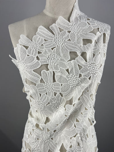 A white mannequin adorned with intricately designed Anglaise Lace - White - 128cm by Super Cheap Fabrics, showcasing large floral patterns ideal for bridal wear. The plain gray backdrop enhances the delicate texture and detail of the lace, making it an exquisite piece for home décor enthusiasts.