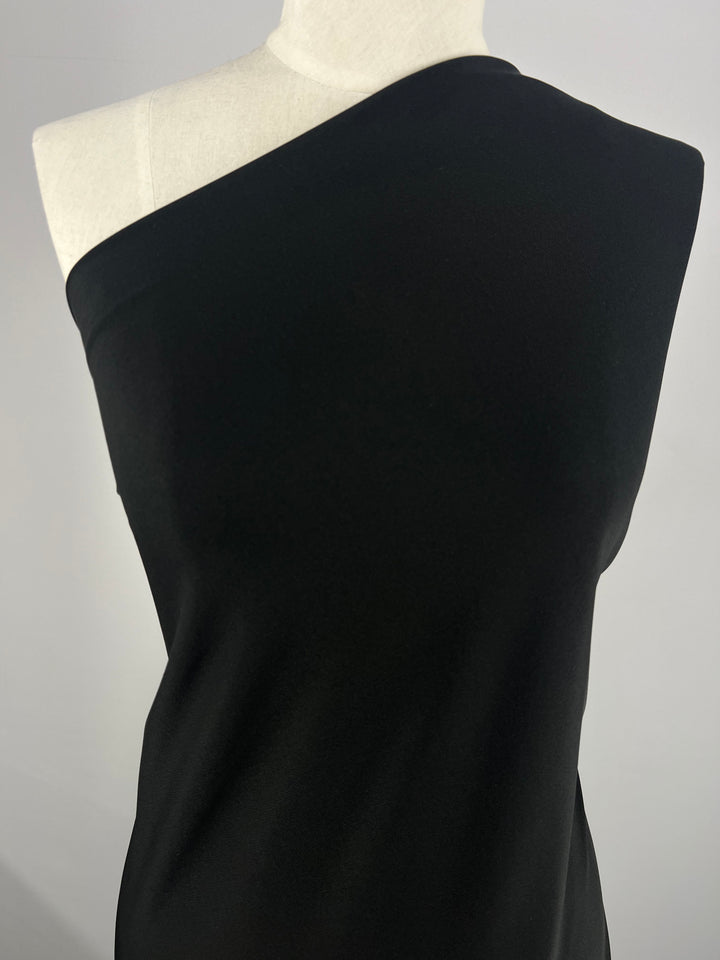 A mannequin elegantly displays a black one-shoulder dress made from the luxurious "Double Knit Jersey - Black- 150cm" by Super Cheap Fabrics, set against a plain white background.