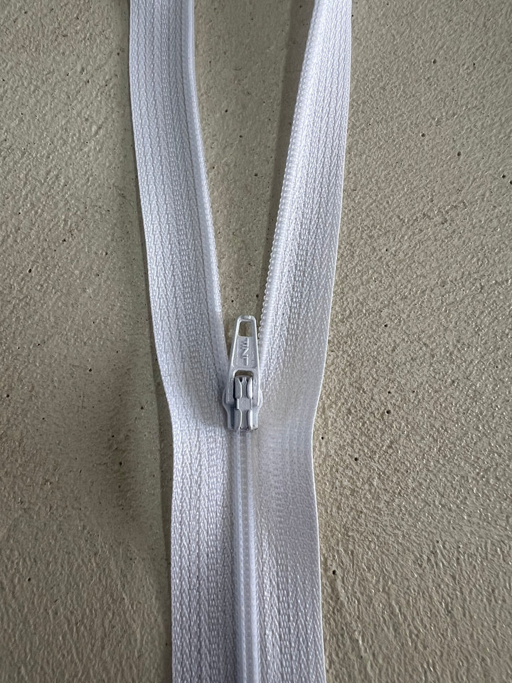 Close-up of the 37cm White Zip by Super Cheap Fabrics, crafted from durable polyester on a textured beige surface, shown partially zipped with the slider near the center.