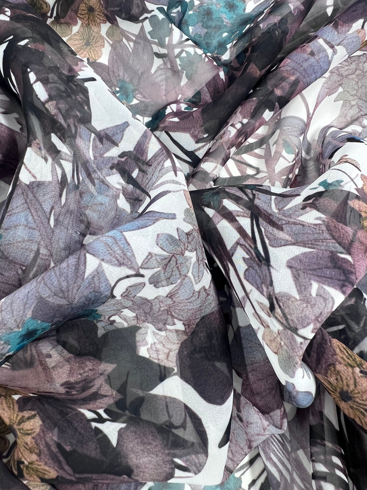 A close-up of the Super Cheap Fabrics' Printed Chiffon - Amazonas shows sheer, lightweight fabric adorned with delicate flowers and leaves in purple, blue, and brown on a white background. It's a soft and intricate design ideal for sewing projects. Width: 150cm.