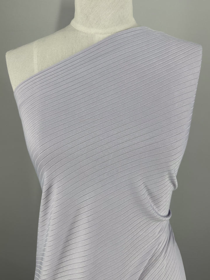 The "Rib Knit - Thistle - 175cm" from Super Cheap Fabrics is showcased on a mannequin against a neutral backdrop, with its medium weight stretch fabric draped diagonally to accentuate the textured knit and subtle sheen.