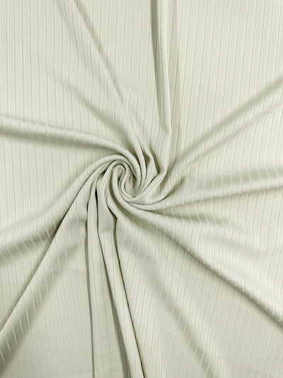 The Rib Knit - Celadon Tint by Super Cheap Fabrics features a close-up of pale green ribbed fabric gathered into a central swirl. This stretchy, medium-weight knit shows visible vertical lines for a subtle texture and pattern. Width: 168cm.