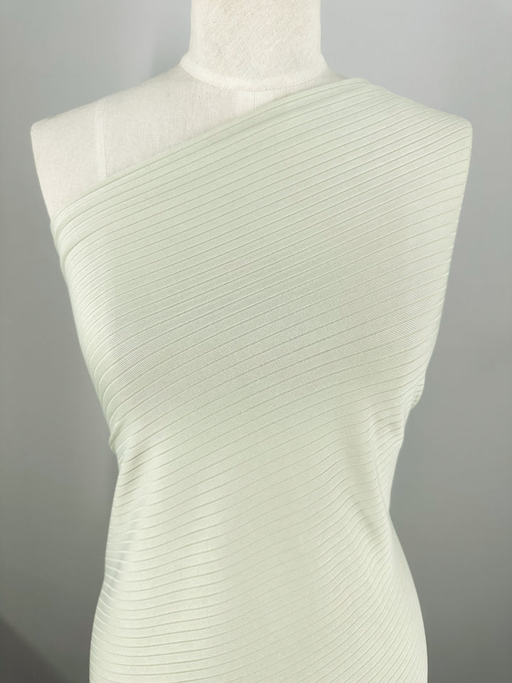 A celadon tint, ribbed, one-shoulder dress made from Super Cheap Fabrics' Rib Knit - Celadon Tint (168cm) is displayed on a mannequin. The medium-weight fabric's textured knit has a subtle sheen, highlighting its elegance and stretch against a plain background.