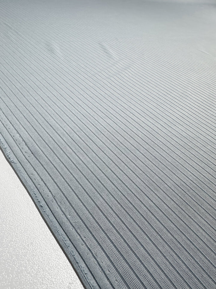 A close-up of Super Cheap Fabrics' Rib Knit in Pearl Blue showcases a smooth, modern texture with evenly spaced horizontal grooves. The lighting accentuates the subtle shadows across the 170cm wide material, enhancing its sleek appearance.