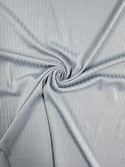 Close-up of the Pearl Blue Rib Knit by Super Cheap Fabrics, showcasing a spiral twist at its center. The medium weight fabric features textural flow with subtle sheen enhancing its ribbed pattern, all within a 170cm width.