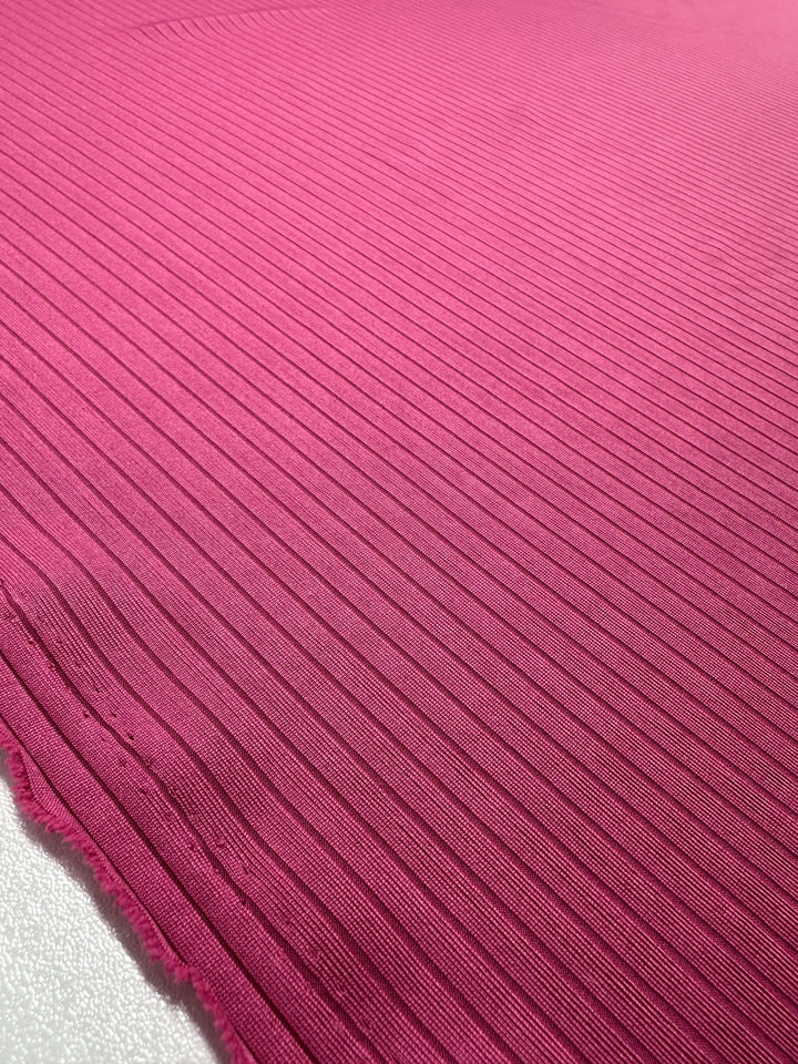 Close-up of Super Cheap Fabrics' Rib Knit in Lilac Rose, 170cm wide, highlighting its magenta ribbed texture with horizontal lines, slightly frayed edge, and soft stretch for comfort.