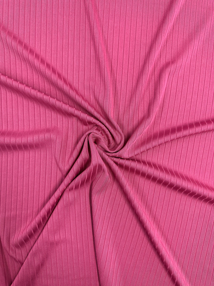 A close-up of Super Cheap Fabrics' Rib Knit in Lilac Rose (170cm) shows the medium weight fabric's swirl pattern with vertical lines. The pink fabric has a soft, flowing texture that emphasizes its stretch and comfort.