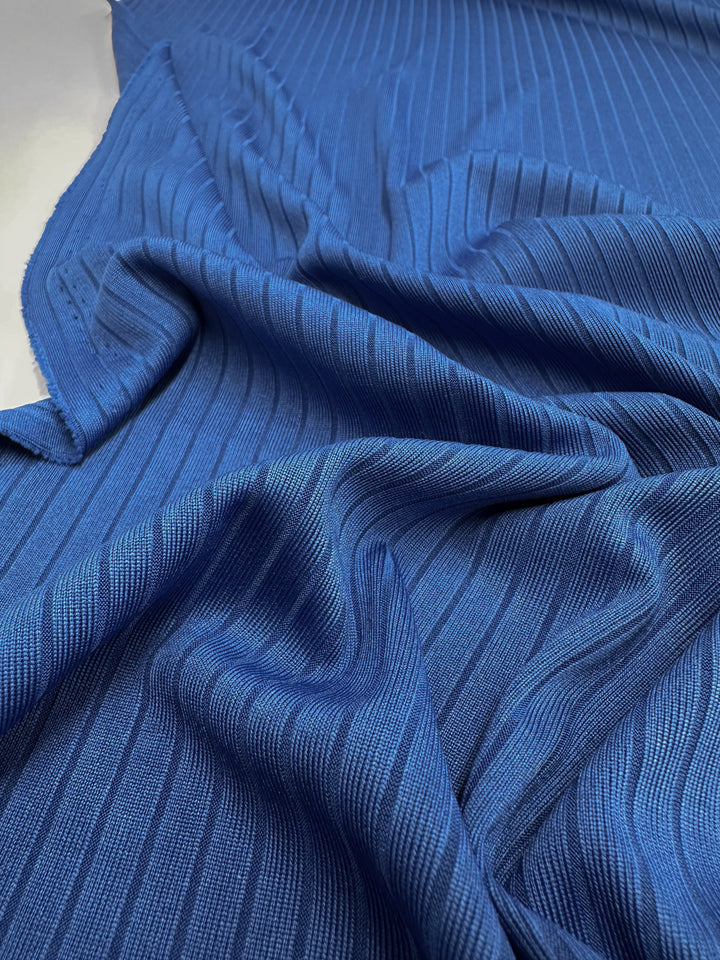 Close-up of Super Cheap Fabrics' Rib Knit - Classic Blue - 170cm, featuring vertical ribbed stripes. The crumpled medium-weight fabric folds create soft shadows, showcasing its generous stretch and adding depth to the surface.