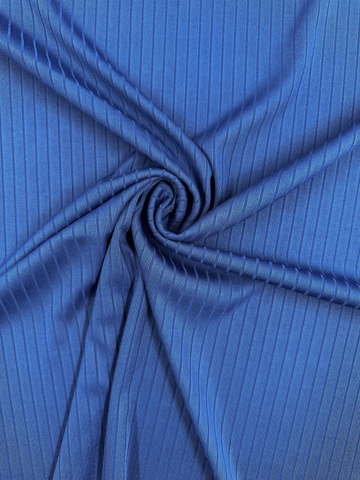 A close-up of the Rib Knit - Classic Blue by Super Cheap Fabrics, 170cm wide. This medium-weight fabric has faint vertical lines that create a textured look and generous stretch, swirled into a circular pattern at the center.